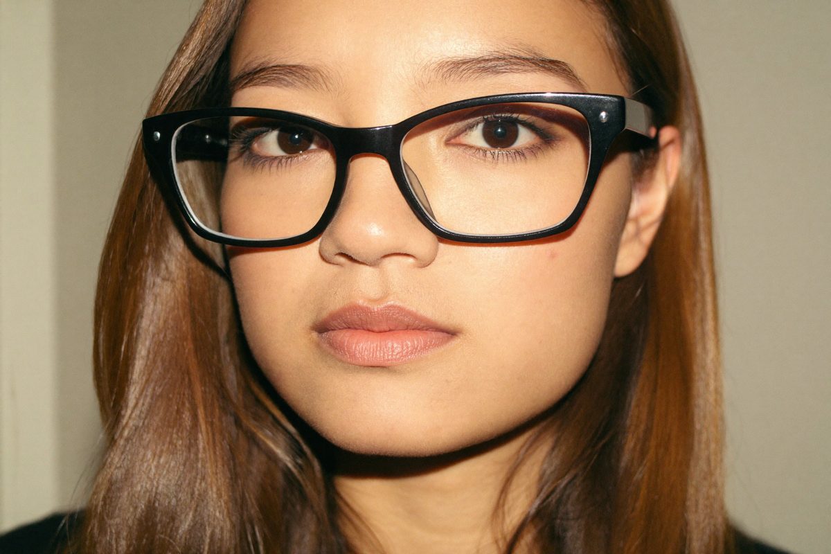 Woman with a round face wearing angular wayfarer-style glasses frames that add definition