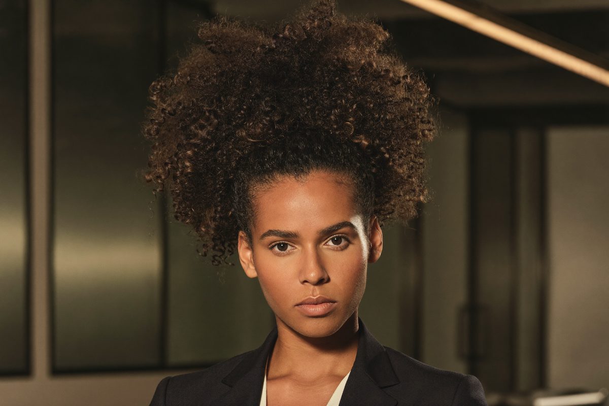 Woman with natural curly hair pulled back neatly into a polished professional style, curls left defined