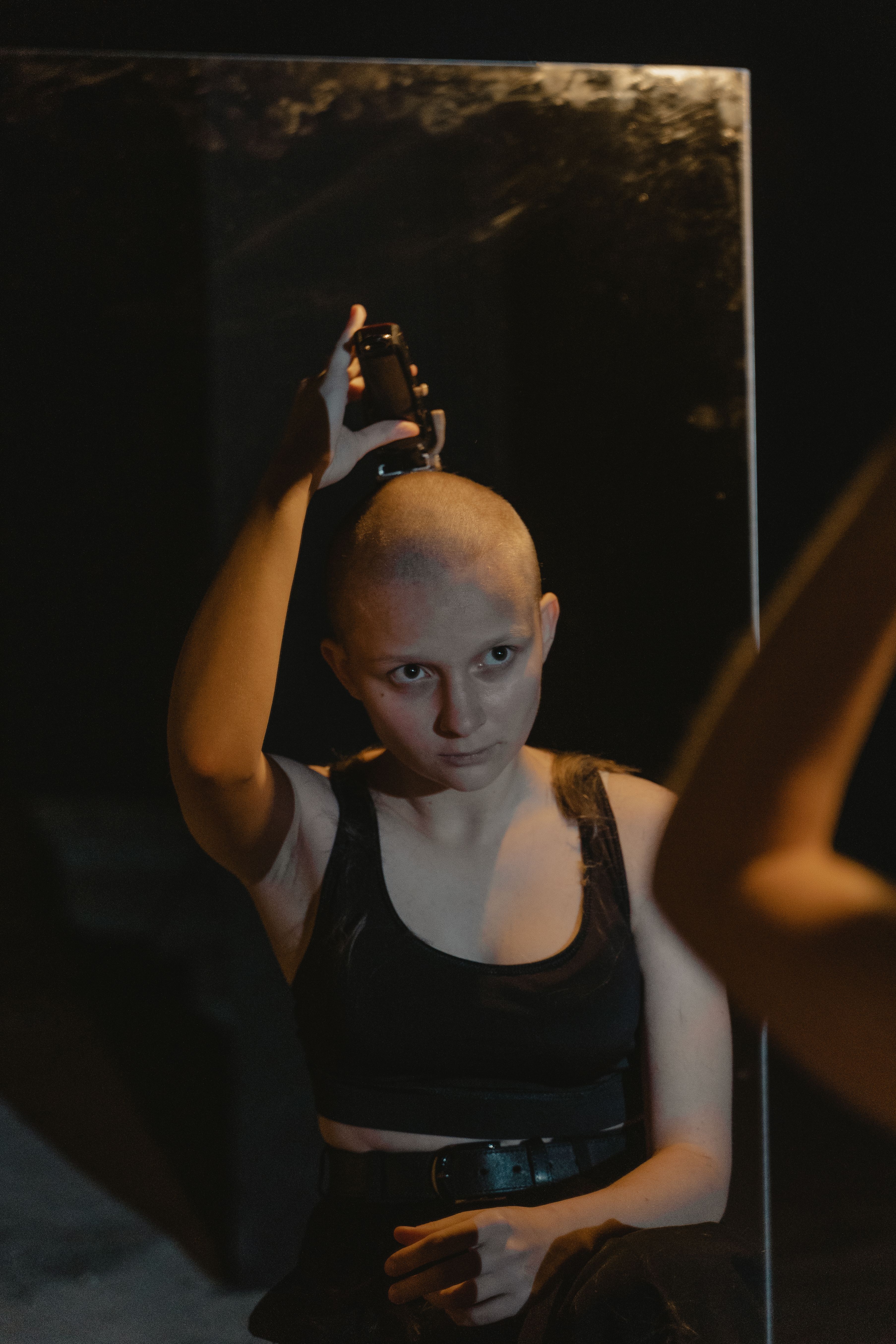 Woman shaving the side of her head in front of a mirror during undercut maintenance