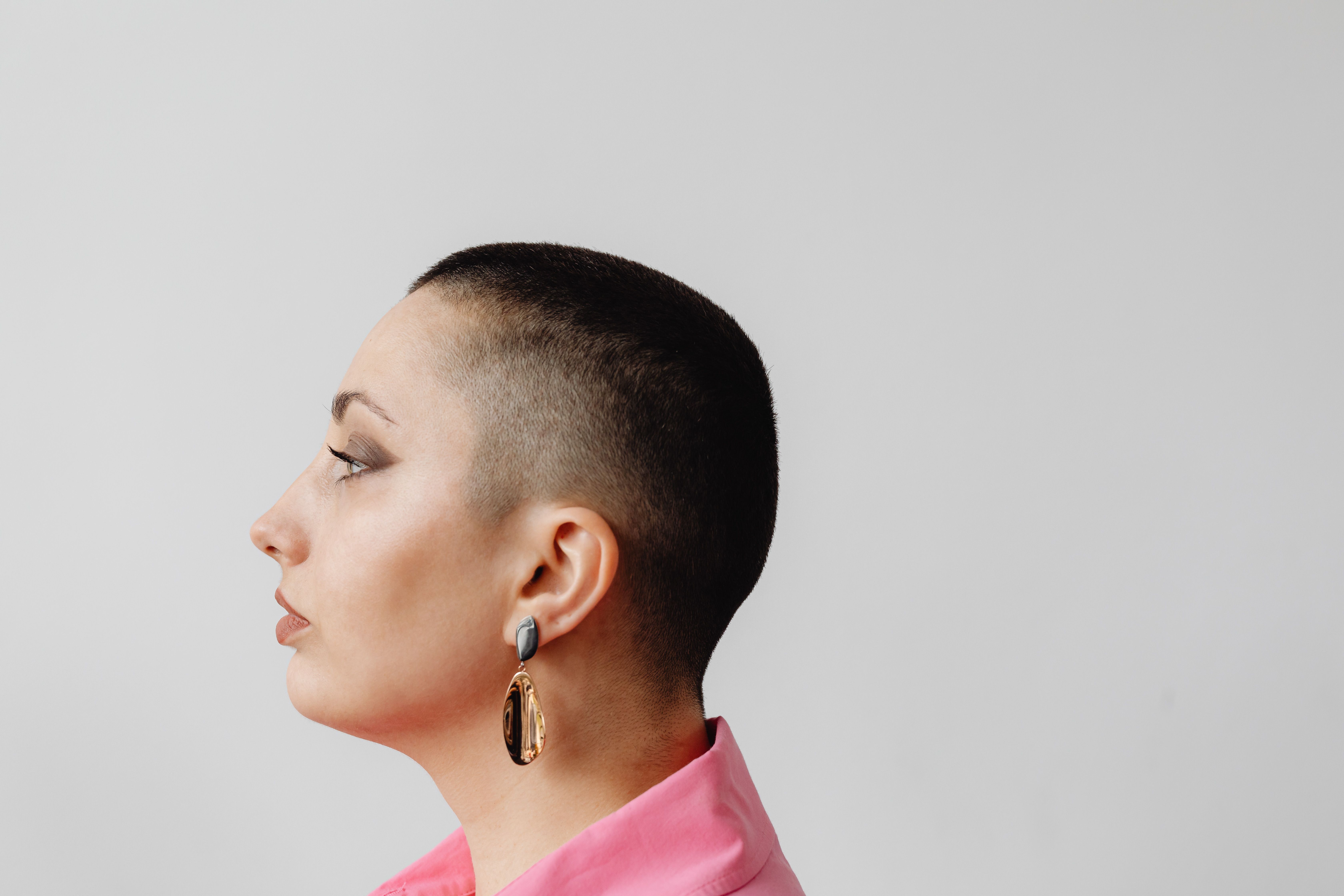 Profile view of a woman with a shaved side and nape undercut and a hoop earring against a neutral background